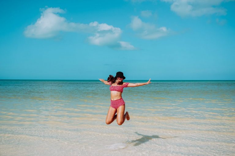 Vrouw springt in de lucht op een strand met helder blauw water in een rode bikini