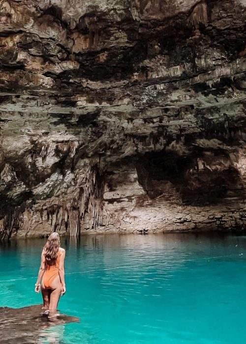 Vrouw staat op de rand van een houten platform omgeven door blauw water en een rotswand met stalactieten in Cenote Xux'Ha in Yucatan Mexico