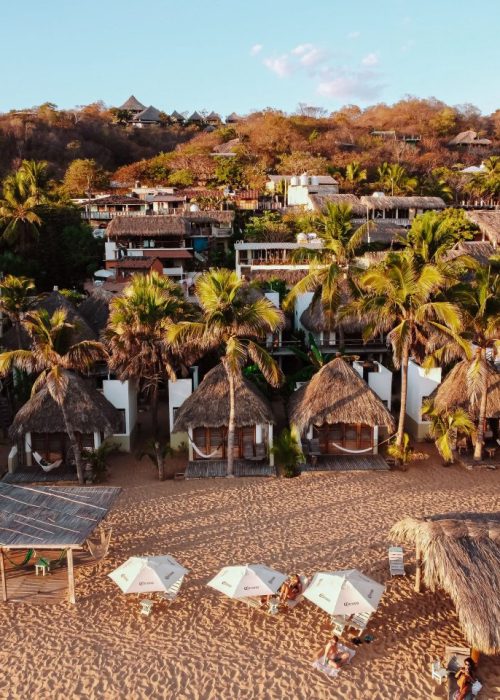 Drone shot van een strand in Mexico met palmbomen en bamboo hutjes